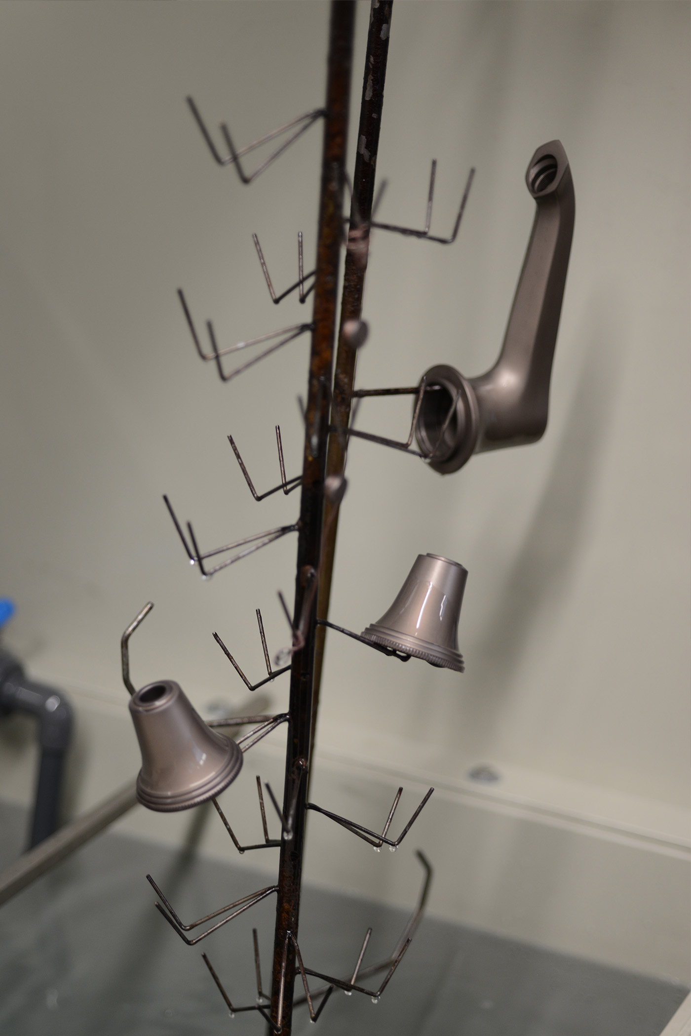 A basin spout and side valve parts on a jig being lifted from a rinse bath to rinse excess dye