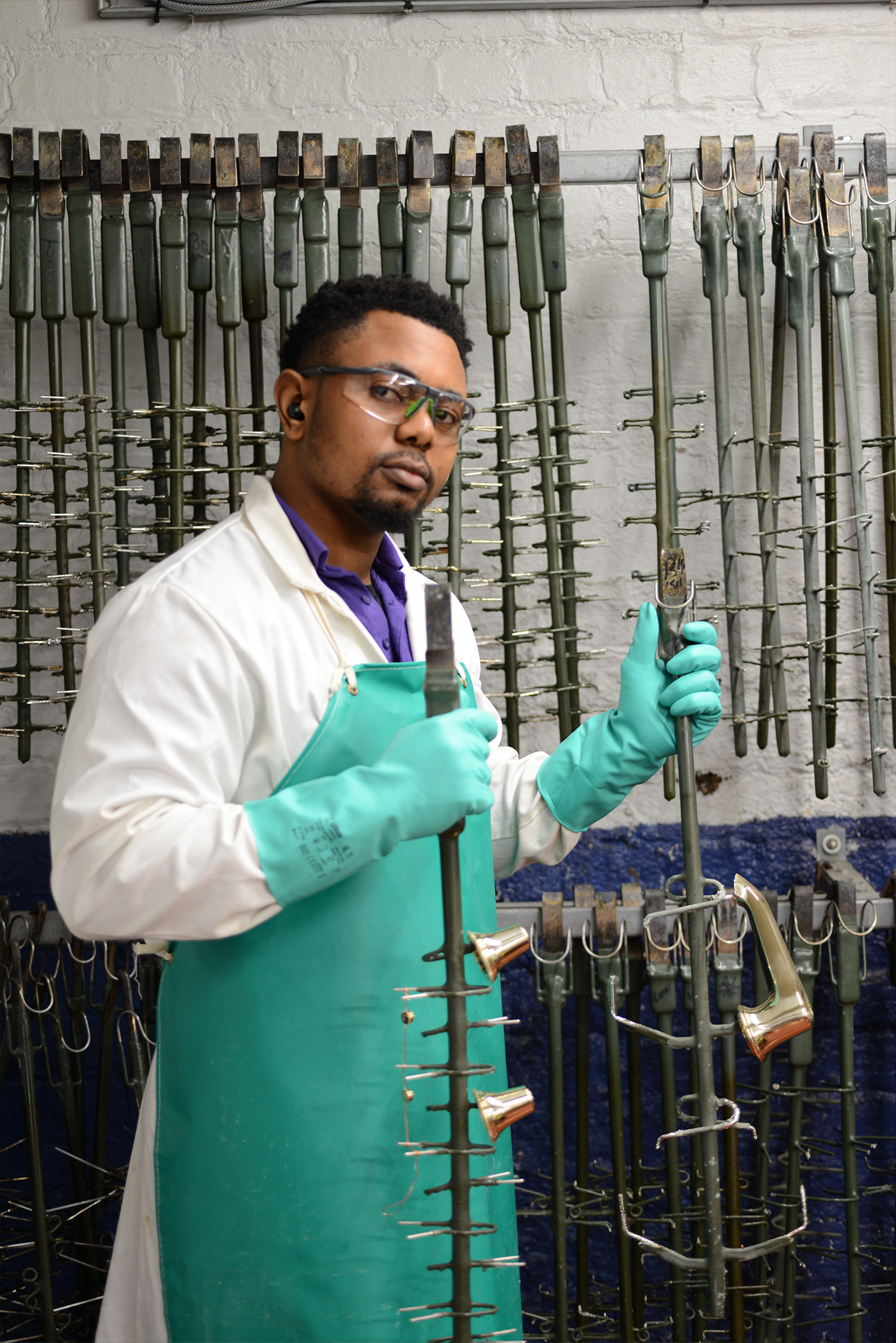 A person holding a jig with a basin spout and side valve parts ready to begin plating in the Samuel Heath electroplating shop