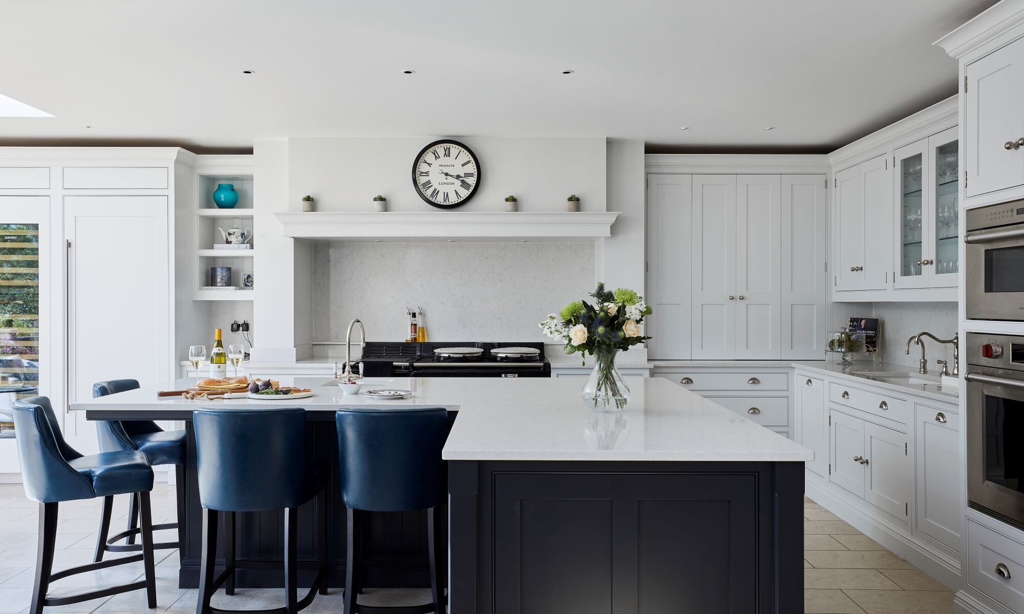 A white kitchen with blue chairs and a clock.