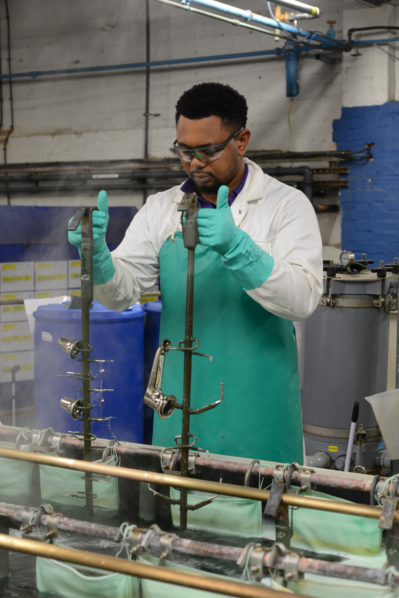 A person electroplating a basin spout and side valve parts in nickel for a durable and smooth base